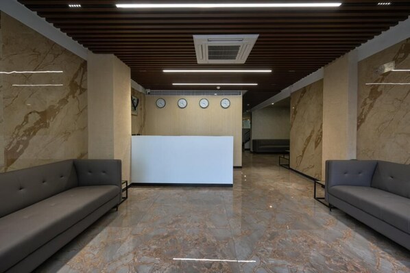 A reception area with marble floors, two sofas, a reception desk, and a ceiling with wooden slats and recessed lighting.