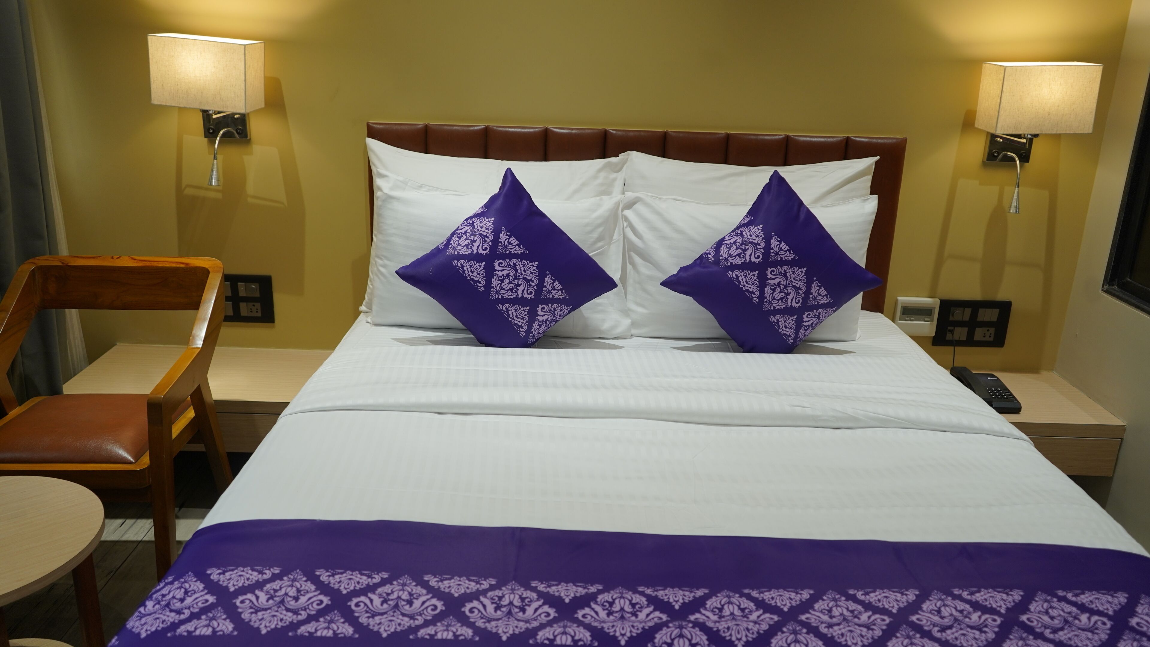 Una habitación de hotel con una cama, dos mesitas de noche, una silla y una lámpara.