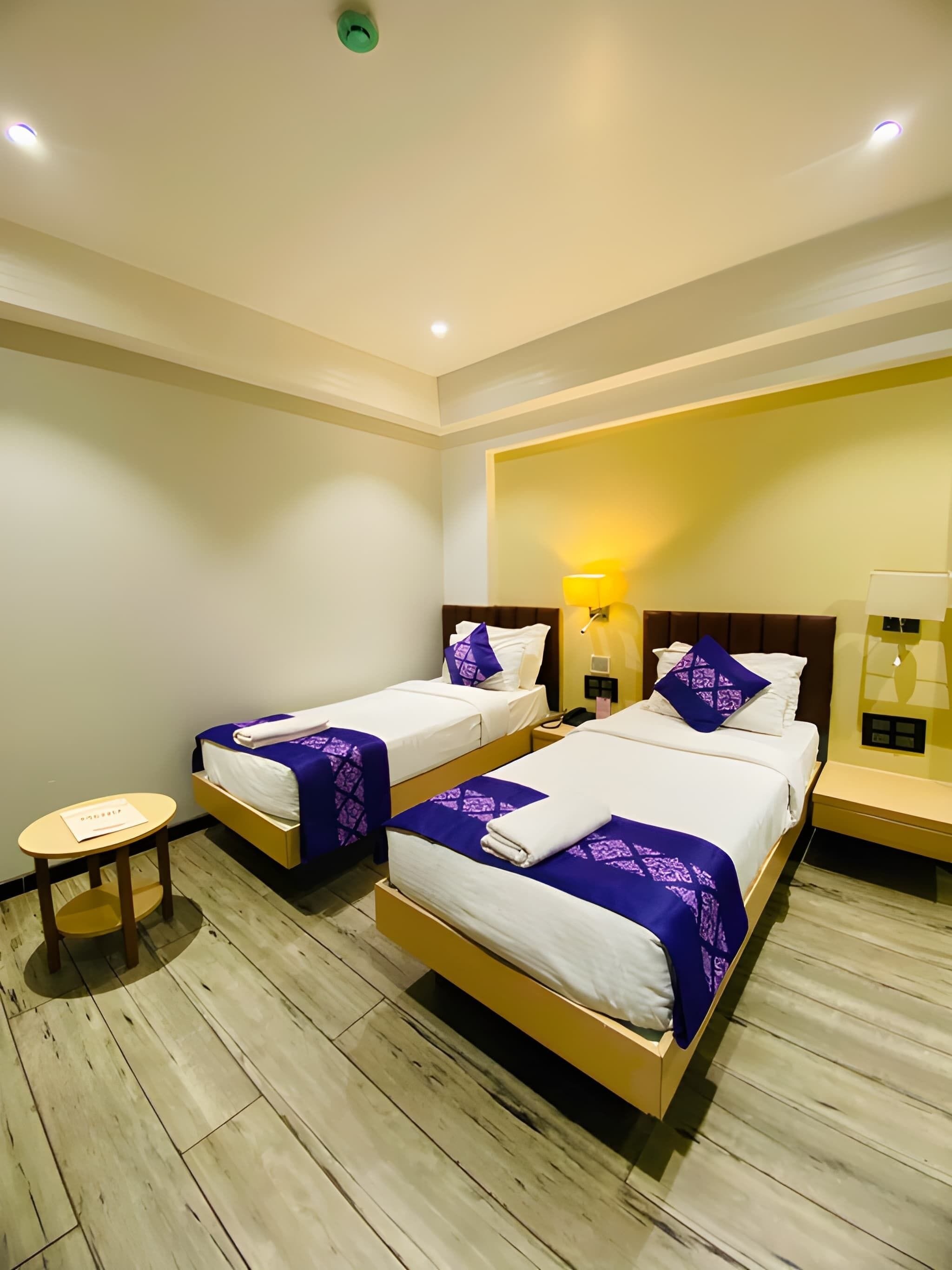 A hotel room with two beds, a small table, and a bedside lamp.