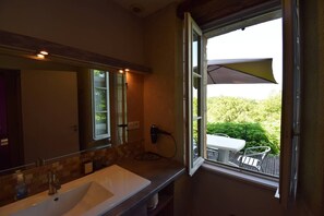 Une salle de bain avec un grand miroir, un lavabo blanc et une fenêtre donnant sur un patio.
