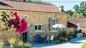Un bâtiment en pierre avec un toit en tuiles, des sièges en plein air avec des chaises colorées et un chemin de gravier.