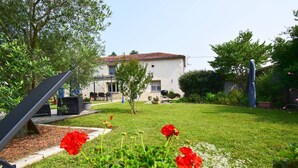 A garden with a lawn, red flowers, and a building with a tiled roof. - Gîte l'Ostalet de Sarron avec piscine, Brax - Lot et Garonne (BRAX)