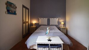 Habitación de hotel estrecha con cama, dos lámparas de noche, una mesita con un adorno y una pared con un cuadro enmarcado y un cartel.