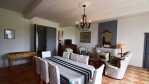 Una habitación con una mesa de comedor, sillas, un sofá, chimenea, televisor y candelabro.