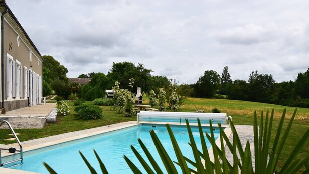 Una piscina rectangular con solárium de hormigón, rodeada de césped y árboles.
