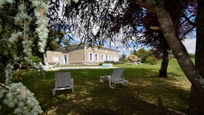 Una casa con jardín y dos sillones blancos.