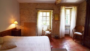A bedroom with a bed, a nightstand, a wooden wardrobe, a chair, and a window with curtains. - Gîte en pleine nature, au cœur du Lot-et-Garonne (LAROQUE TIMBAUT)