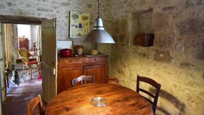A rustic dining area with a wooden table and chairs, a hanging lamp, and a stone wall. - Gîte en pleine nature, au cœur du Lot-et-Garonne (LAROQUE TIMBAUT)