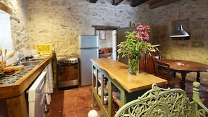 A rustic kitchen with stone walls, a wooden table, and a refrigerator. - Gîte en pleine nature, au cœur du Lot-et-Garonne (LAROQUE TIMBAUT)