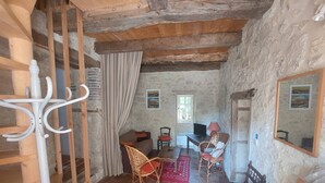 A rustic room with a stone wall, wooden beams, a wooden coat rack, a dining table with chairs, and a television. - Gîte en pleine nature, au cœur du Lot-et-Garonne (LAROQUE TIMBAUT)
