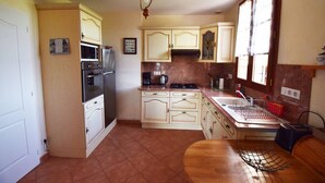 A compact kitchen with wooden cabinets, a stove, a sink, and a dining table. - Gîte avec piscine à Madaillan, Lot-et-Garonne (MADAILLAN)