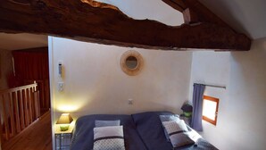 A bedroom with a wooden ceiling beam, a round mirror, two beds with patterned bedding, a nightstand with a lamp, and a window with curtains. - Gîte avec piscine à Madaillan, Lot-et-Garonne (MADAILLAN)