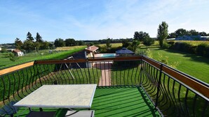 A pool area with a table and chairs, surrounded by a fence and a view of a house and fields. - Gîte avec piscine à Madaillan, Lot-et-Garonne (MADAILLAN)