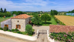 A stone house with a tiled roof, surrounded by a gravel driveway and a metal gate. - Gîte avec piscine à Madaillan, Lot-et-Garonne (MADAILLAN)