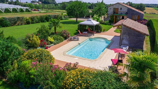 A swimming pool with a patio area, surrounded by lush greenery and a stone house. - Gîte avec piscine à Madaillan, Lot-et-Garonne (MADAILLAN)