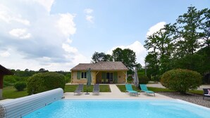 An outdoor swimming pool with lounge chairs and umbrellas, a small building with a tiled roof, and a well-maintained lawn. - Gîte avec piscine et jacuzzi - Lot-et-Garonne (BLANQUEFORT SUR BRIOLANCE)