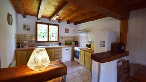 A kitchen with wooden beams, a window with curtains, a lamp, and basic appliances. - Gîte avec piscine et jacuzzi - Lot-et-Garonne (BLANQUEFORT SUR BRIOLANCE)