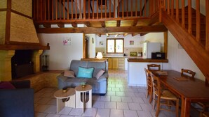 A spacious living area with a wooden staircase, a sofa, a dining table, and a kitchen in the background. - Gîte avec piscine et jacuzzi - Lot-et-Garonne (BLANQUEFORT SUR BRIOLANCE)