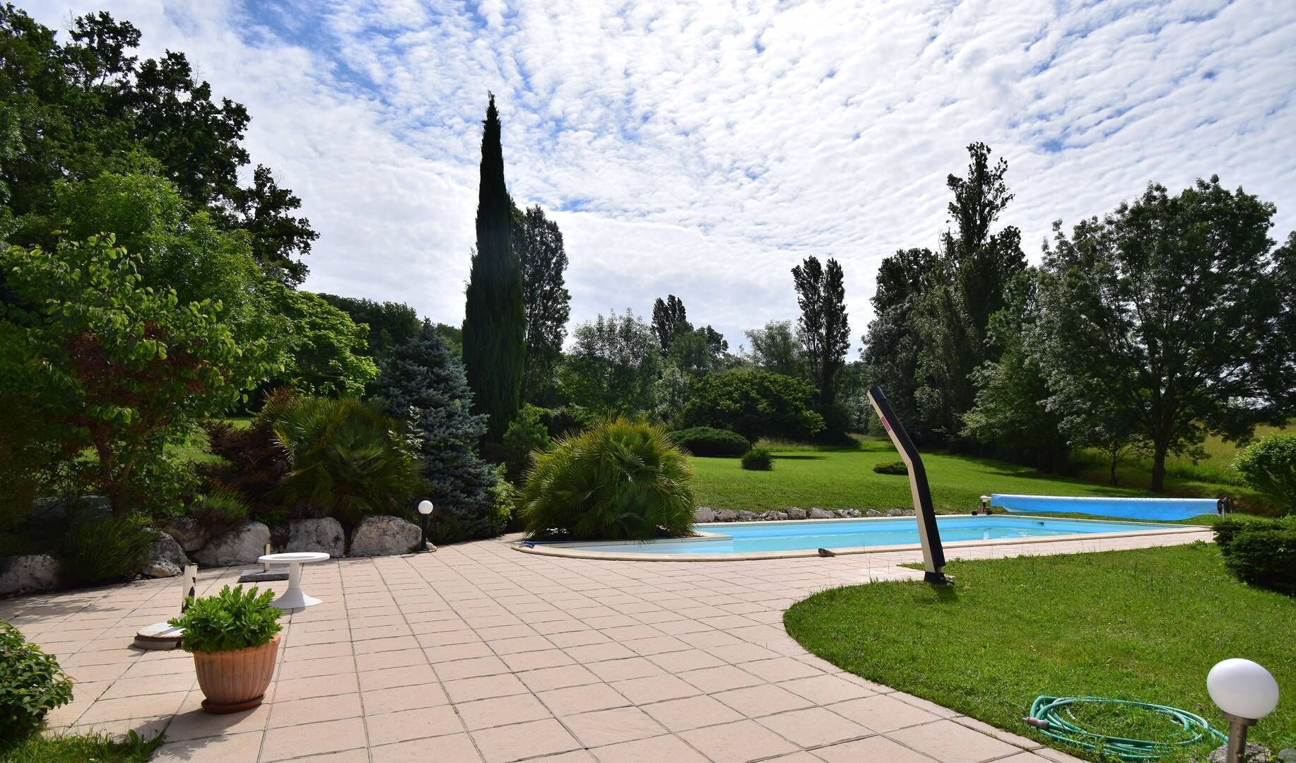 Un jardin aménagé avec une piscine, un grand arbre et une pelouse bien entretenue.