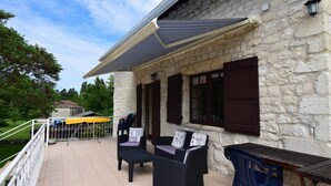 Un edificio in pietra con un portico coperto, mobili da esterno e una pergola dotata di pannelli solari.