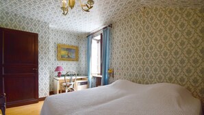 Una camera da letto con un letto grande, un'armadio in legno, una scrivania con una sedia, una finestra con tende e un quadro appeso al muro.