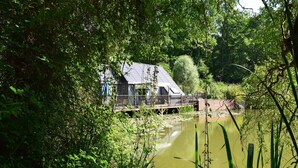 A house with a sloped roof, a wooden deck, and a pond in front.