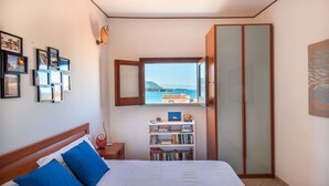 Une chambre à coucher avec un lit, une bibliothèque, une armoire et une fenêtre donnant sur la mer.