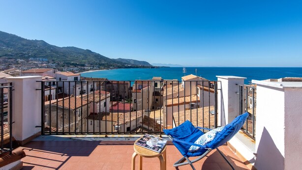 Un balcon avec vue sur la mer, une chaise et une table avec un magazine.