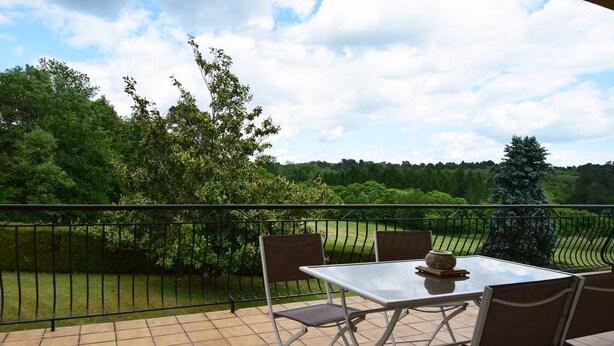Eine Terrasse mit Tisch und Stühlen, einer dekorativen Schale und Blick auf eine grüne Landschaft mit Bäumen und einem Zaun.