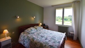 Ein Schlafzimmer mit einem Bett, zwei Nachttischlampen, einem Fenster mit Blick auf Grünflächen und einer Heizung.
