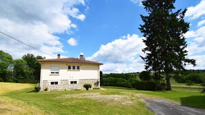 Ein zweigeschossiges Haus mit Steinunterbau und Ziegeldach, umgeben von einem gepflegten Rasen und einem großen Baum.