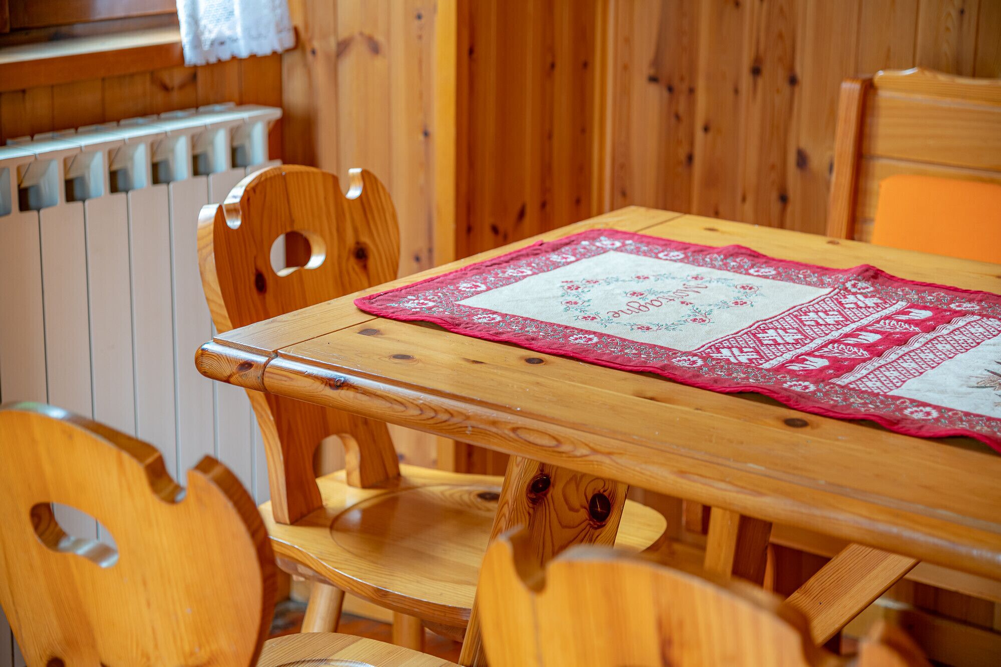 A wooden dining table with a red and white table runner, surrounded by wooden chairs with cut-out backs.