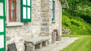 Un edificio de piedra con contraventanas verdes y un banco de piedra afuera.
