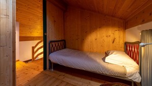 Ein kleines Zimmer mit einem Einzelbett, Holzwänden und einer schrägen Decke.
