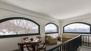 Une pièce comprenant une table à manger et des chaises, un canapé et trois grandes fenêtres en arc de cercle offrant une vue sur les montagnes.