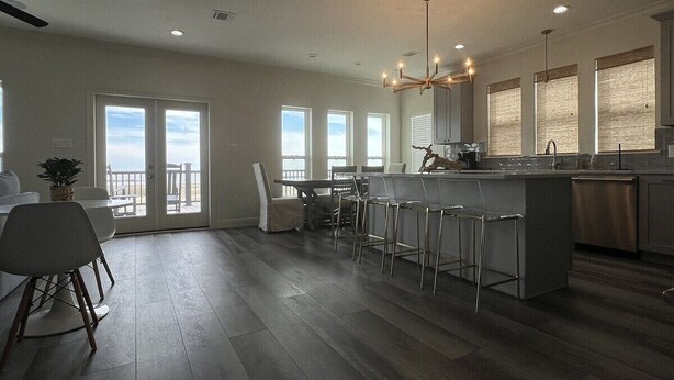A modern kitchen with a central island, bar stools, and a dining area with a table and chairs. - White Dolphin - Beachfront - Island Realty (Grand Isle)