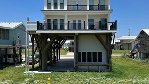 A two-story house with a balcony on the upper floor, a garage on the ground floor, and a small porch area. - White Dolphin - Beachfront - Island Realty (Grand Isle)