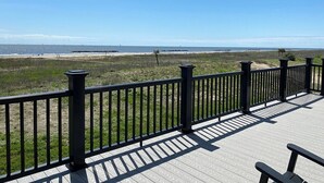 A wooden deck with a black railing overlooking a beach. - White Dolphin - Beachfront - Island Realty (Grand Isle)