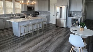 A modern kitchen with a central island, bar stools, stainless steel appliances, and a round dining table. - White Dolphin - Beachfront - Island Realty (Grand Isle)