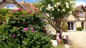 Un jardin où les fleurs sont en pleine floraison et une maison en pierre avec un toit en tuiles.