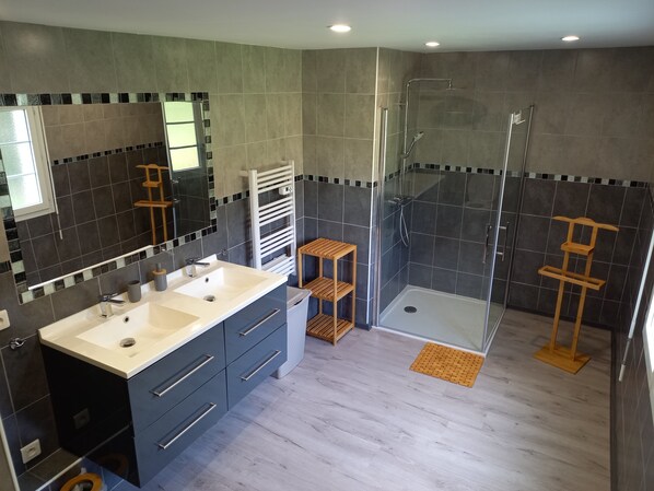 Un baño moderno con dos lavamanos, una cabina de ducha de vidrio y un estante de madera.