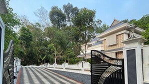 Un camino pavimentado que conduce a una entrada con portón, un portón tradicional y un edificio con techo de tejas y fachada de ladrillo.