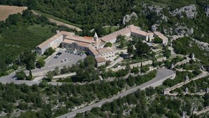 An aerial view of a historic building complex with multiple structures, a parking area, and surrounding greenery. - Villa Piscine vue Castelas (Rochefort-du-Gard)