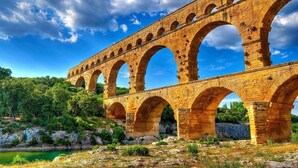 A stone aqueduct with multiple arches over a river, surrounded by greenery and a clear sky. - Villa Piscine vue Castelas (Rochefort-du-Gard)