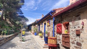 Un étroit sentier de pierre, bordé de bâtiments aux couleurs vives, rouge et bleu, mène à un mur de pierre sur lequel est apposée une plaque.
