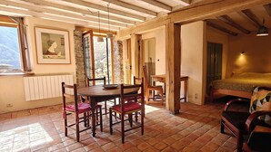 Une pièce rustique comprenant un lit, une table à manger avec des chaises, un mur en pierre et une fenêtre.