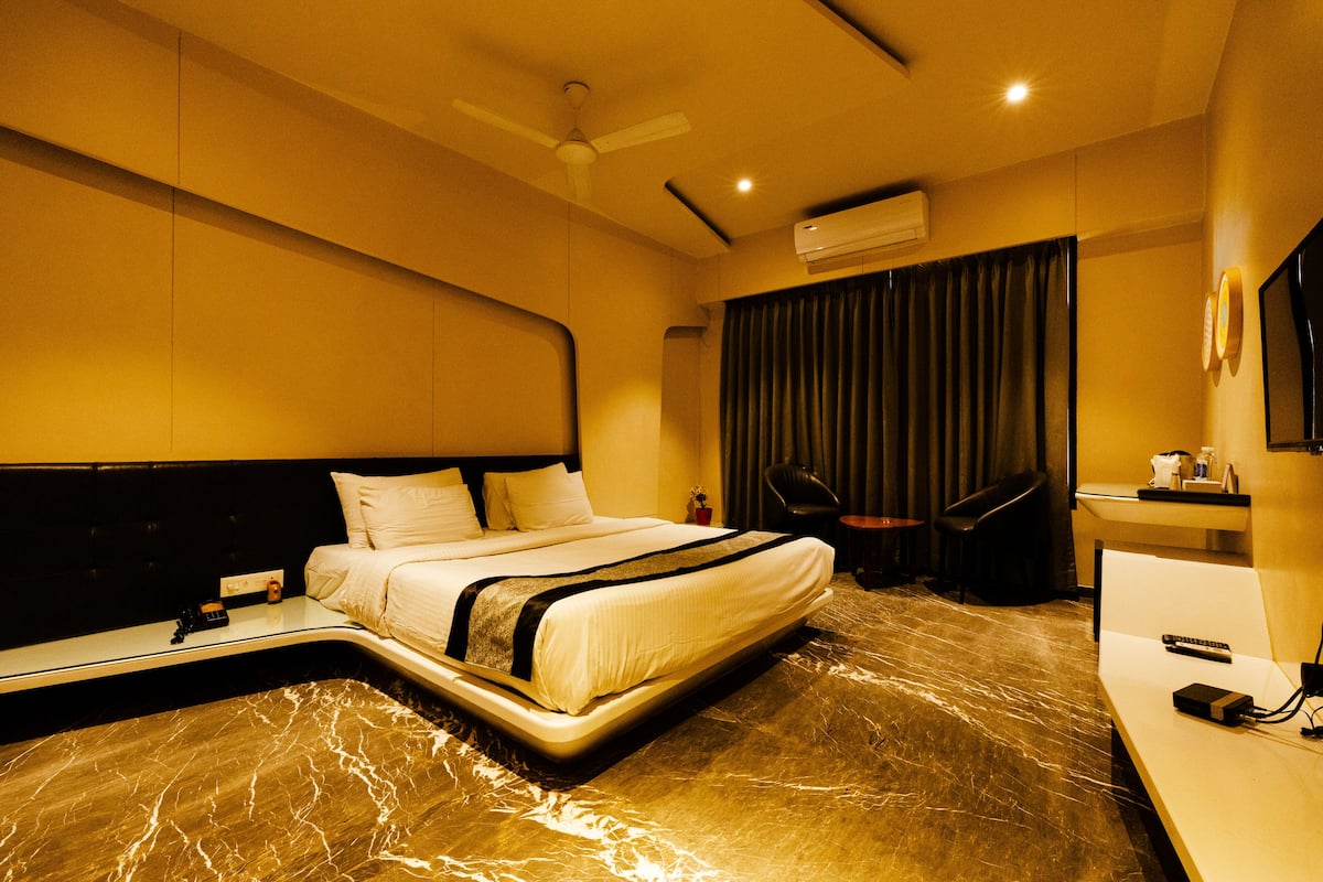 A modern hotel room with a large bed, a desk, a chair, and a flat-screen TV.