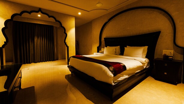 A hotel room with a large bed, a nightstand, a desk, and a chair. - Hotel Brij Residency (Latur)