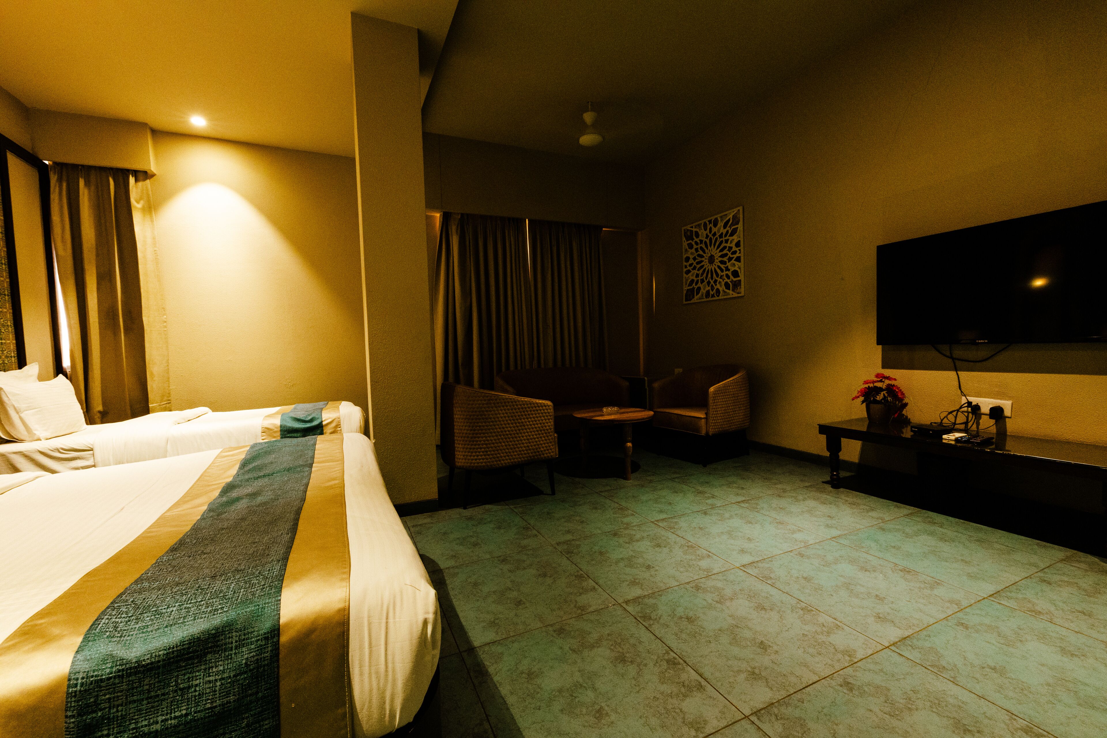 Quarto de hotel com duas camas, um espaço de estar com cadeiras, uma mesinha e uma TV fixada na parede.