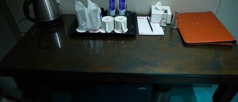 A hotel desk with a kettle, two bottles of water, a tissue box, a notepad, and a pen.